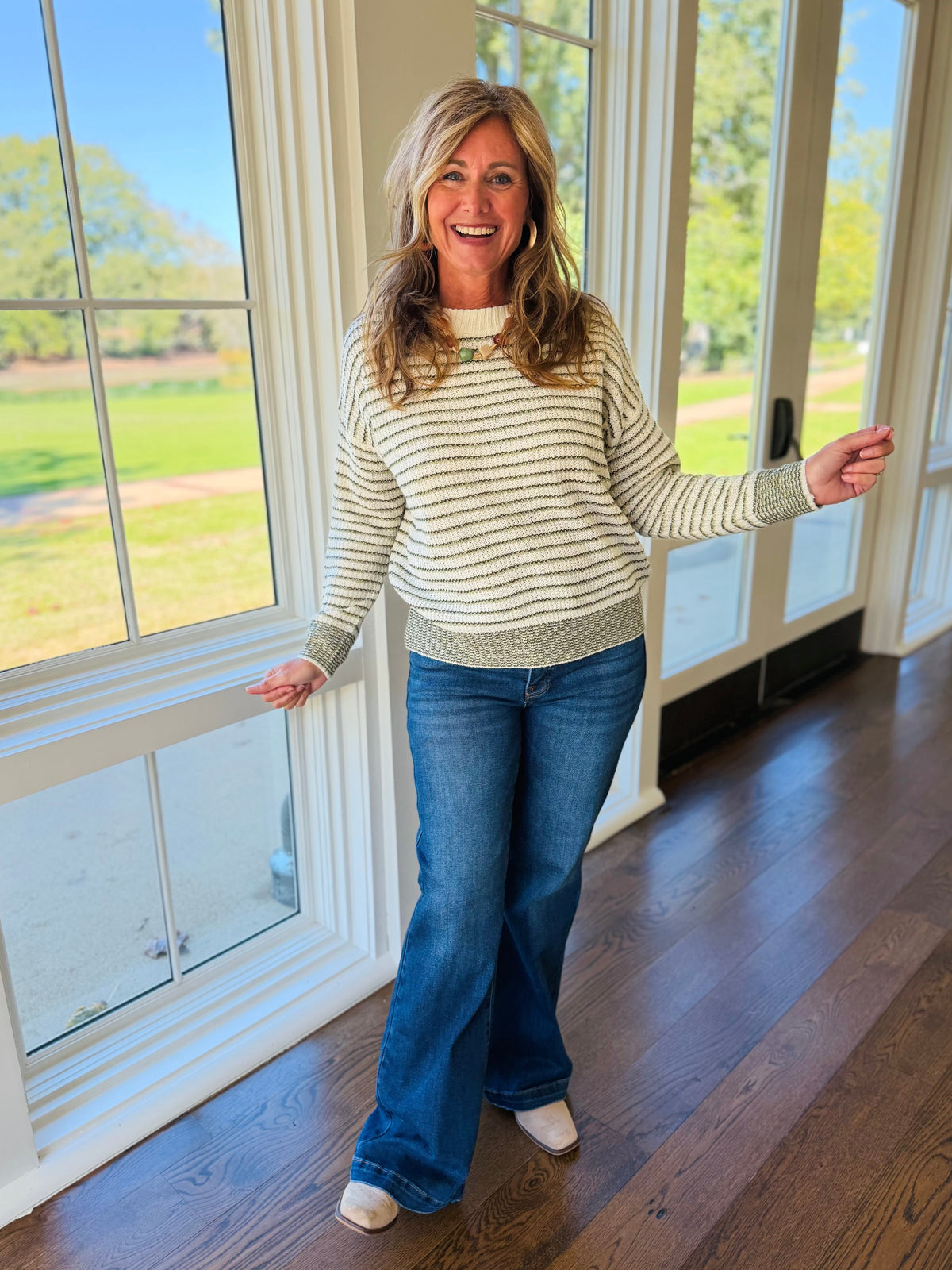 Kelly wearing the Hollis olive striped knit sweater with blue jeans and neutral ankle boots.