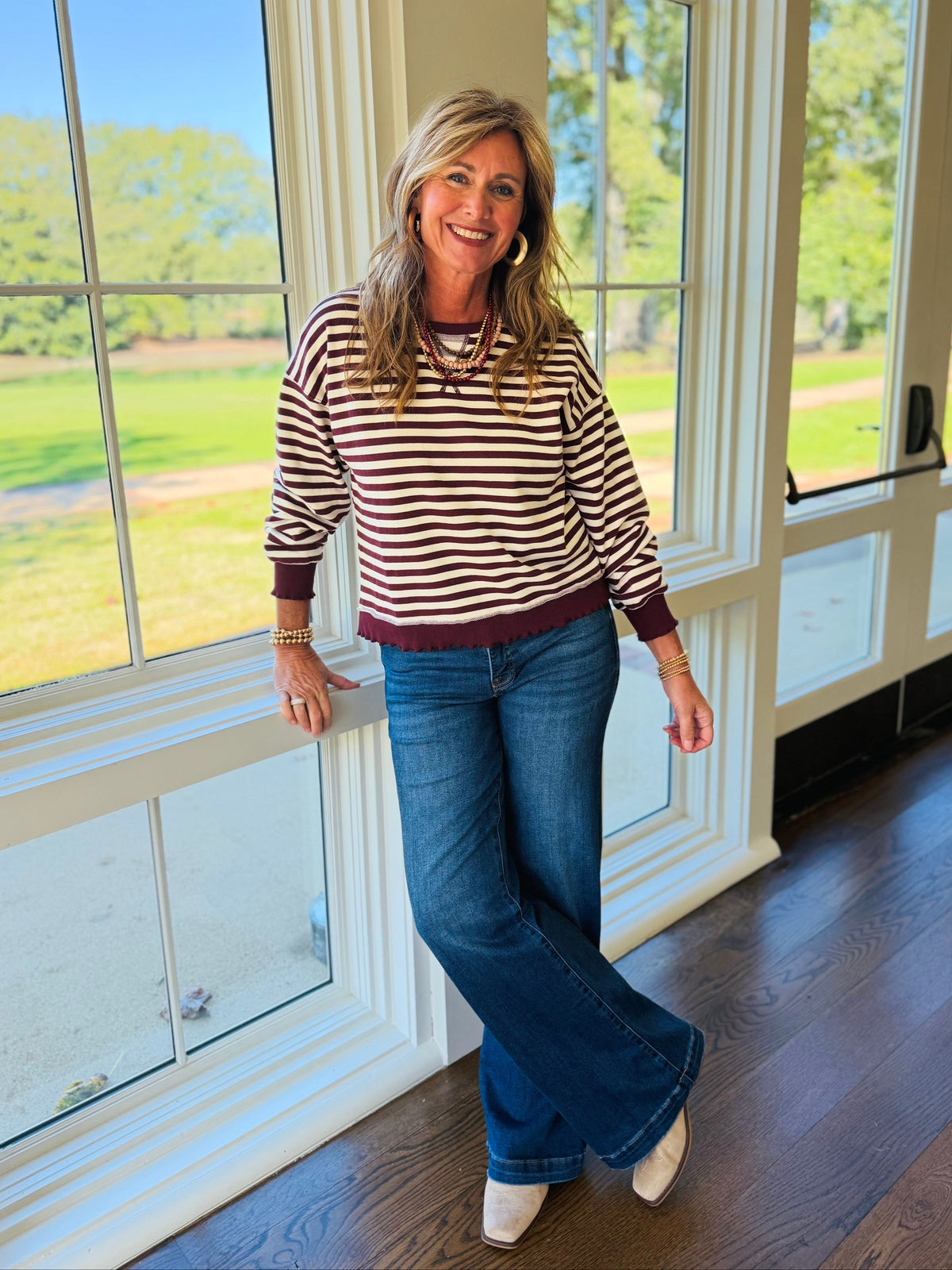 Kelly wearing the Jazlyn burgundy mix striped sweatshirt with blue jeans and neutral ankle boots.