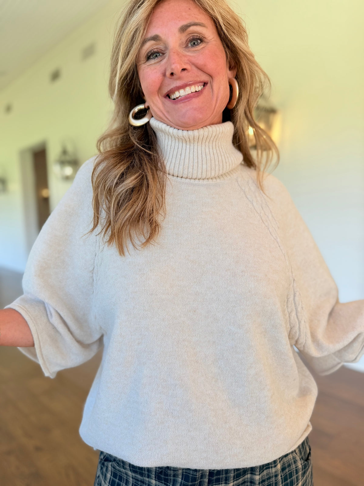 Close-up of the Julianna oatmeal sweater showing its ribbed foldover turtleneck, shoulder cable detailing and wide sleeves.