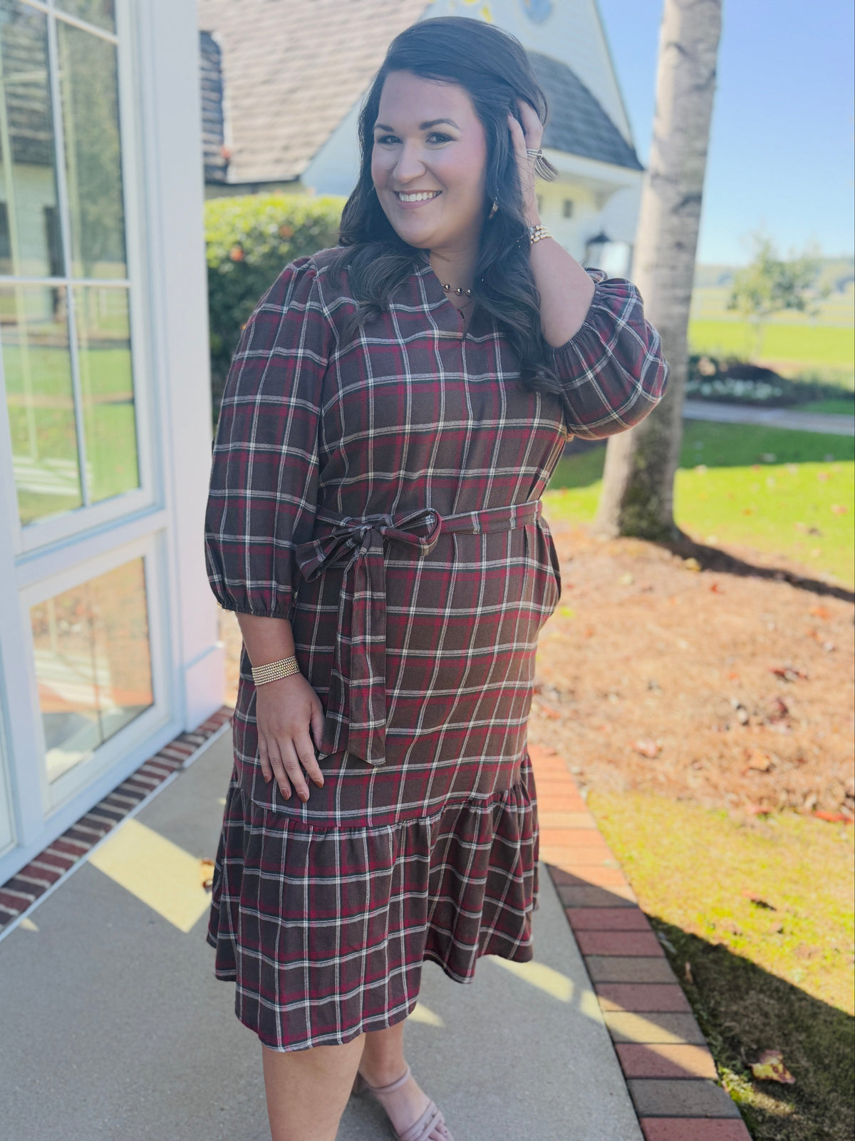 Alex wearing the Kelsey brown plaid belted midi dress with three-quarter sleeves and a ruffled hem.