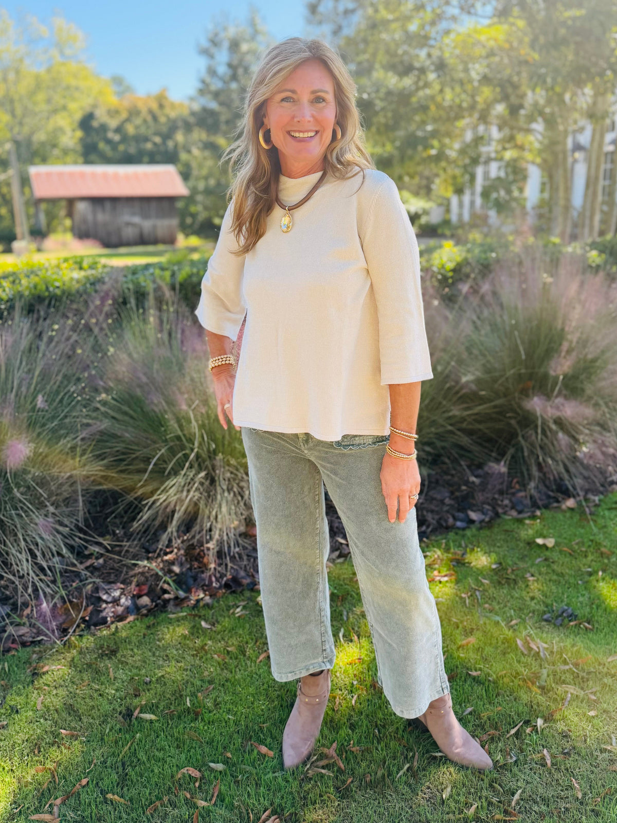 Kelly wearing the Lenora ecru mock neck top with light green cropped pants and taupe ankle boots outdoors.