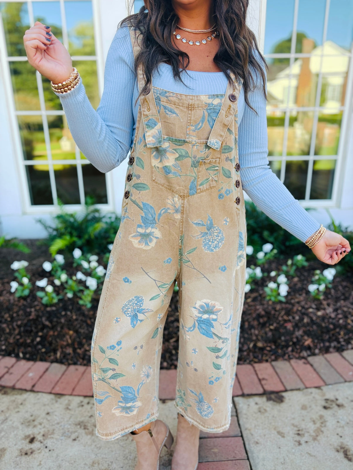 Close-up of the Lucille floral overalls showing their square bib, adjustable button straps, side buttons and front pocket.