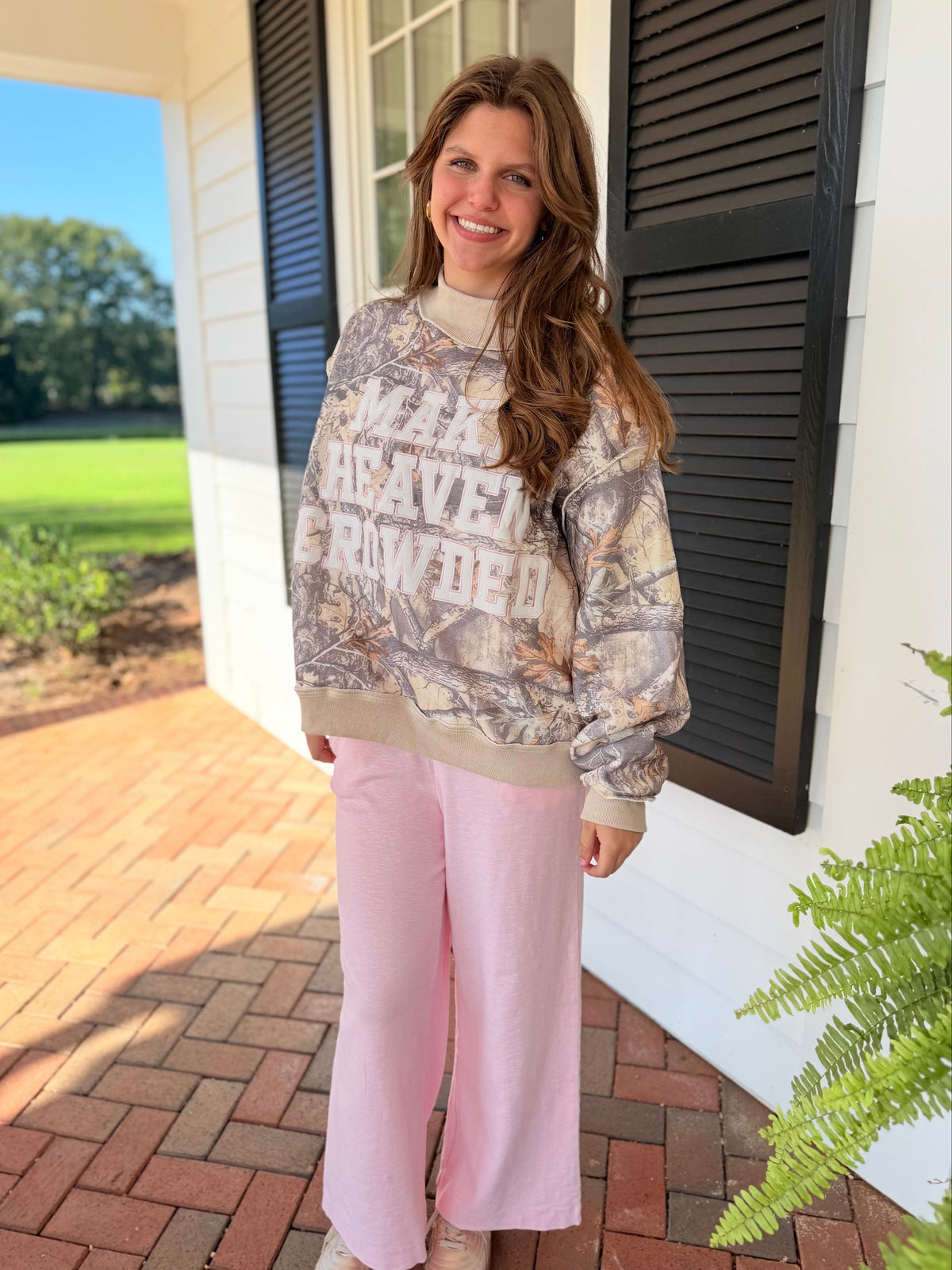 Gade wearing the Make Heaven Crowded camo mock-neck sweatshirt with soft pink wide-leg pants and neutral shoes.