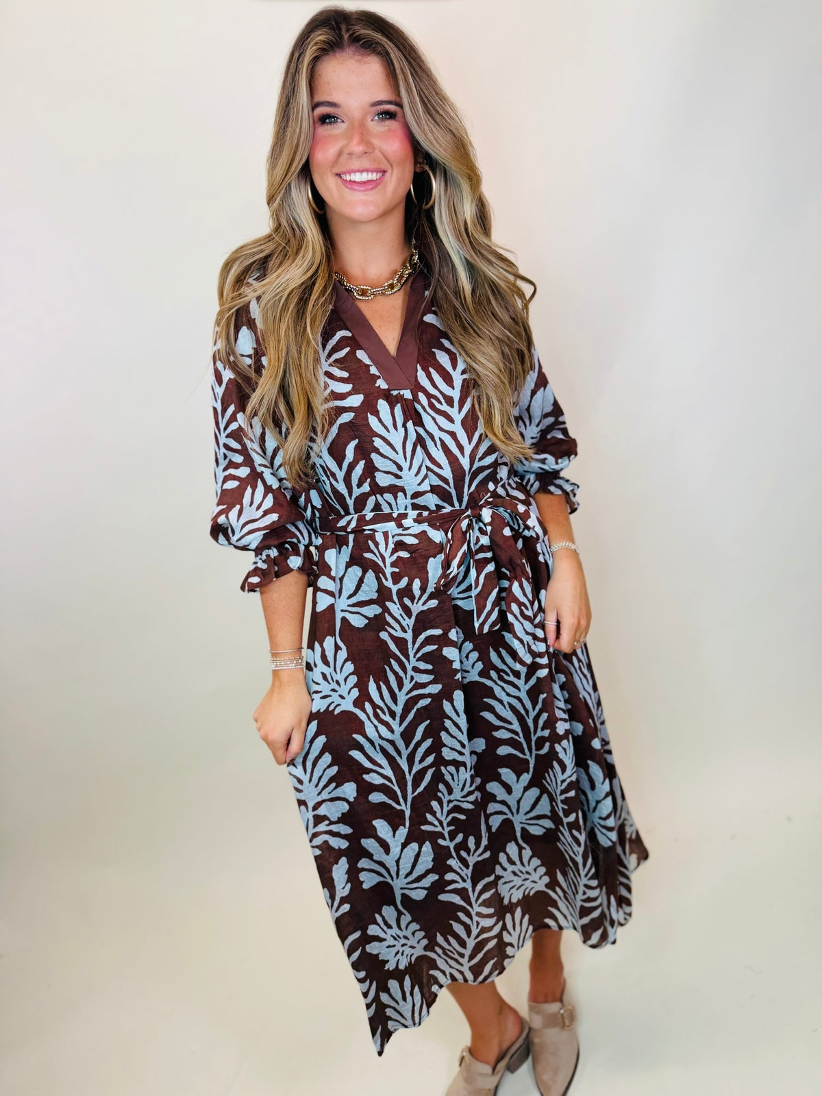 Model wearing the Mason brown and light blue botanical midi dress with a tie waist, V-neck, and three-quarter sleeves.