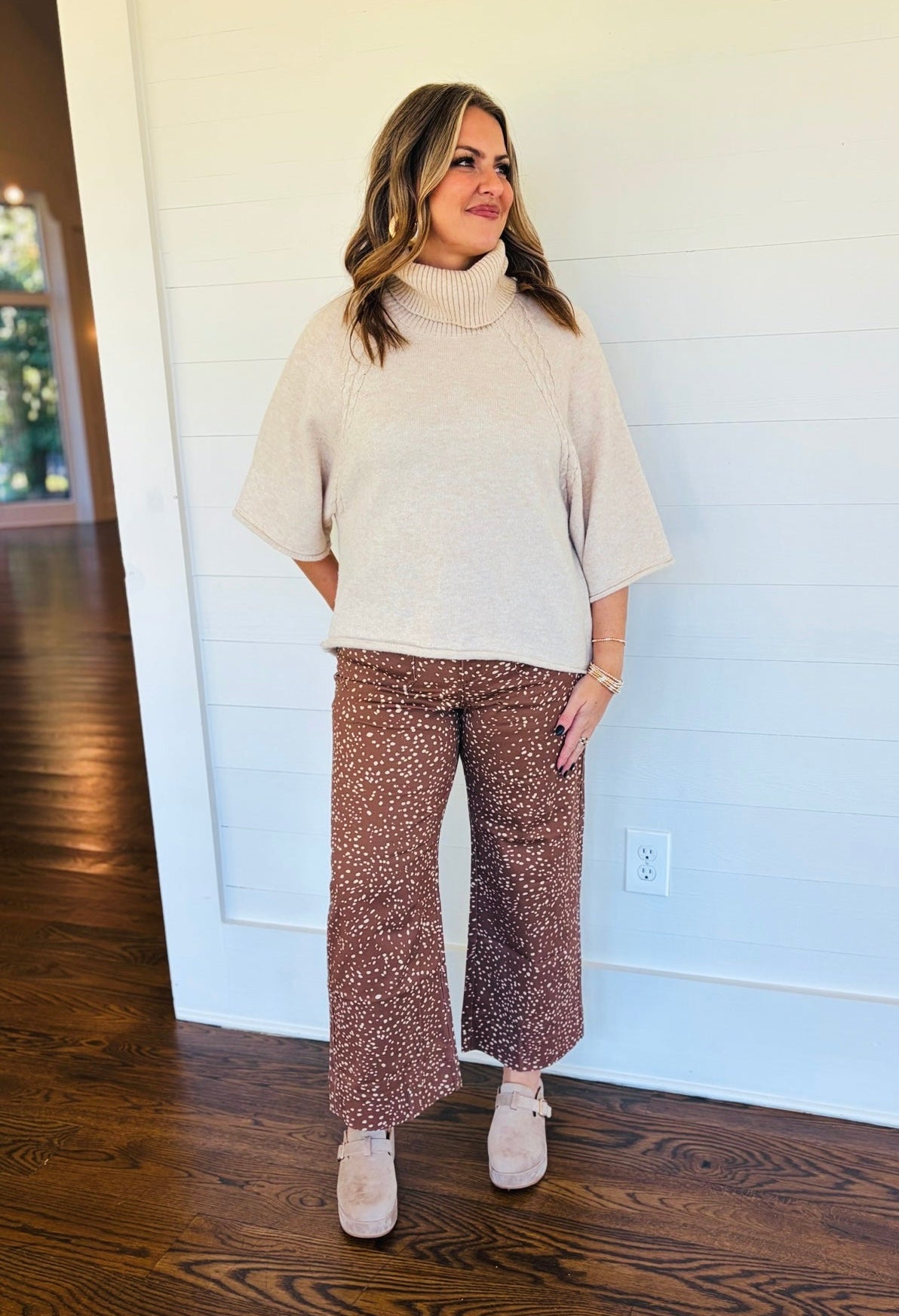 Jessica wearing the Mila brown speckled wide-leg pants with a cream turtleneck sweater and taupe platform shoes.