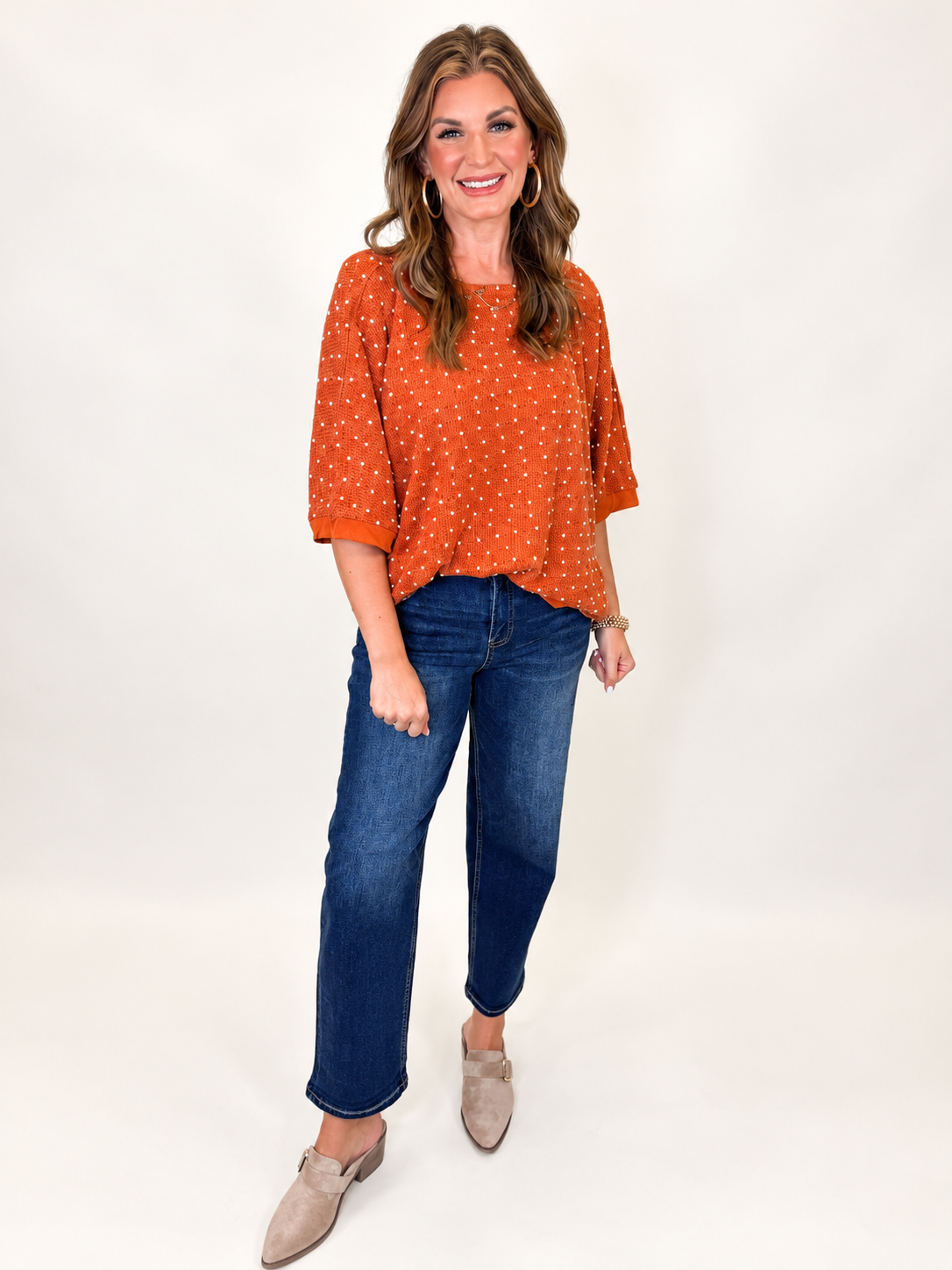 Morgan wearing the Millie rust textured dot knit top with dark blue jeans and neutral loafers.