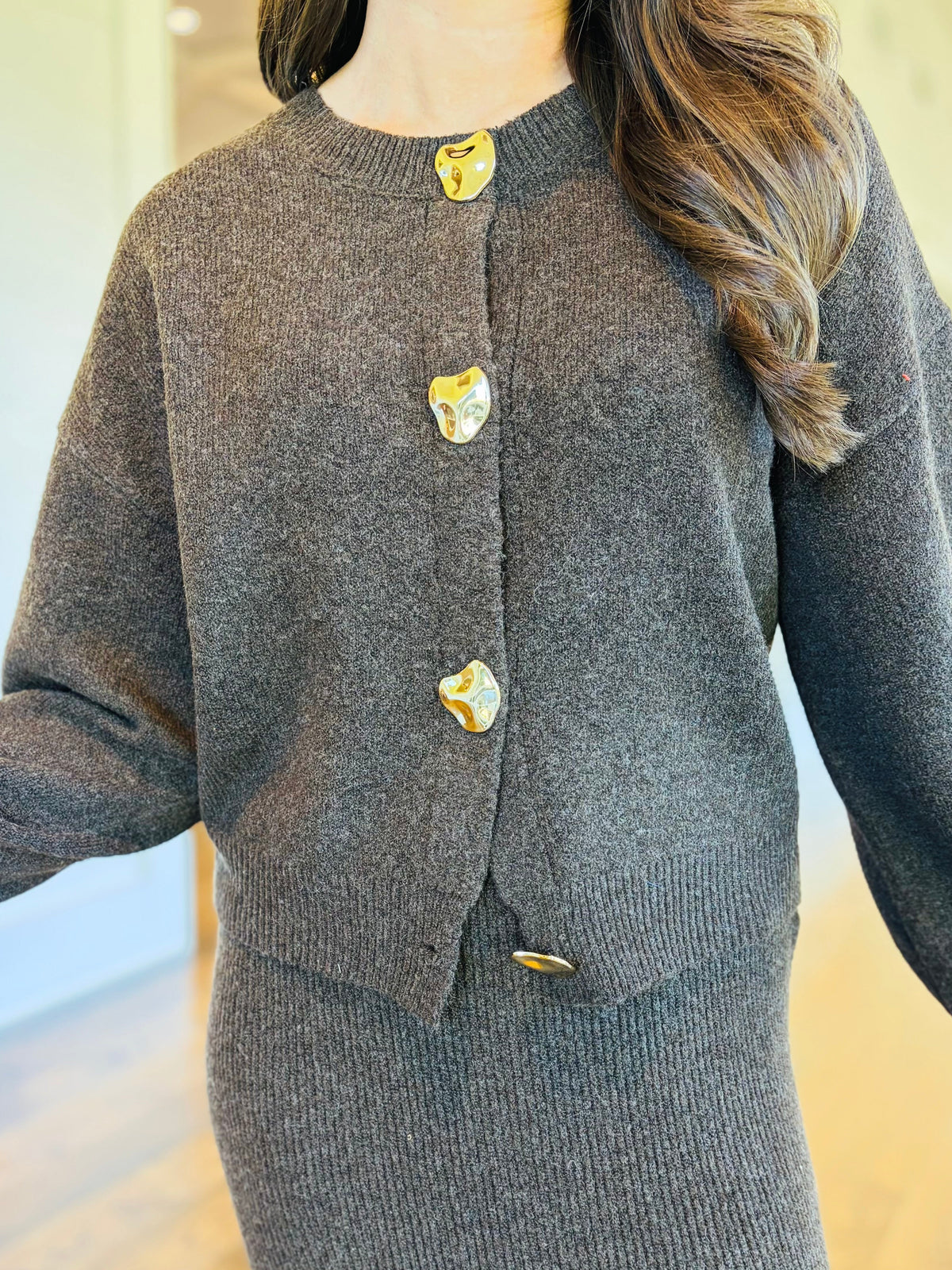 Close-up of the Noelle charcoal brown cardigan showing its round neckline, ribbed knit texture and sculptural gold-tone buttons.