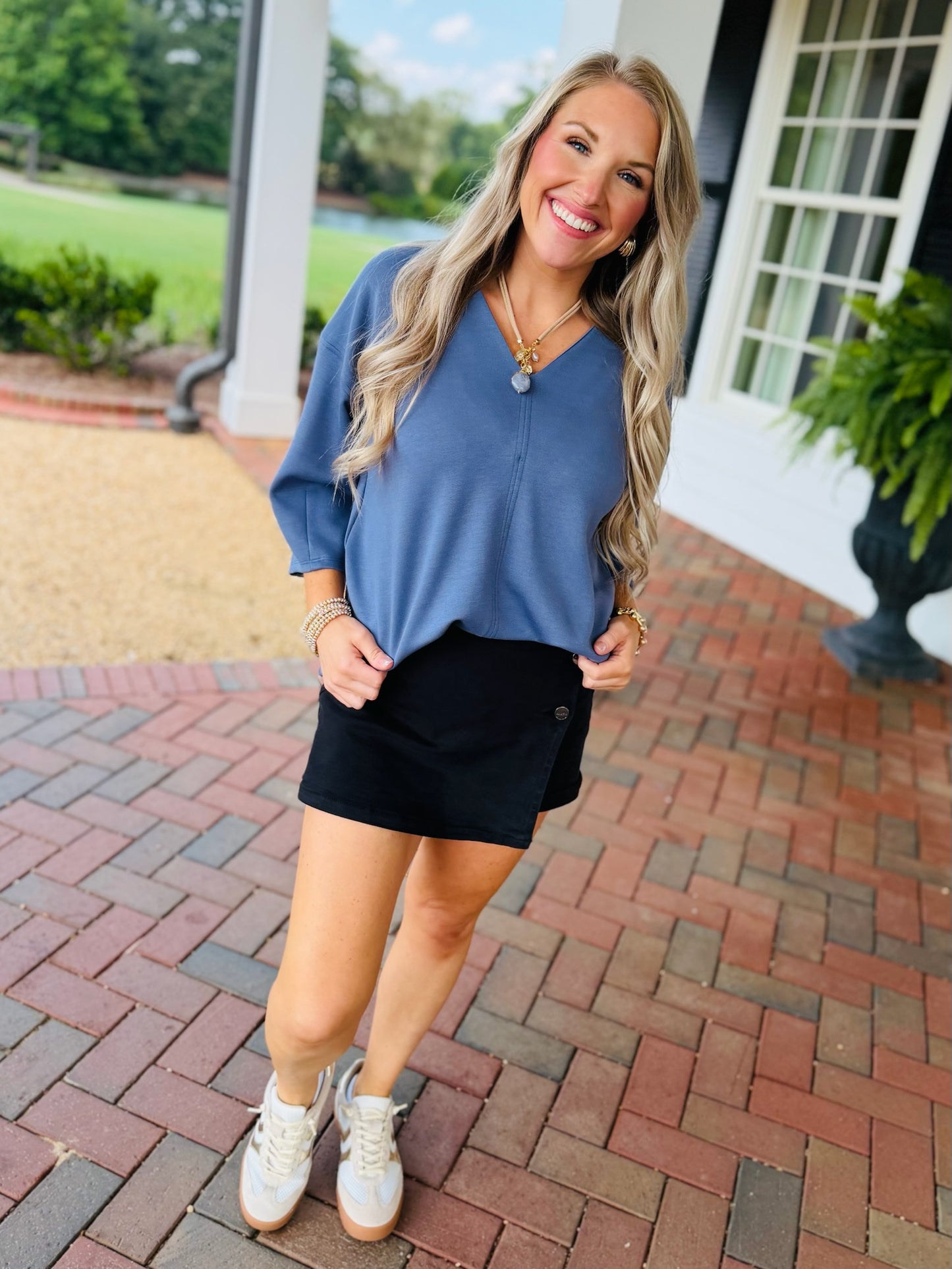 Lorin wearing the Rosalie denim blue V-neck three-quarter-sleeve top with a black wrap skort and white sneakers