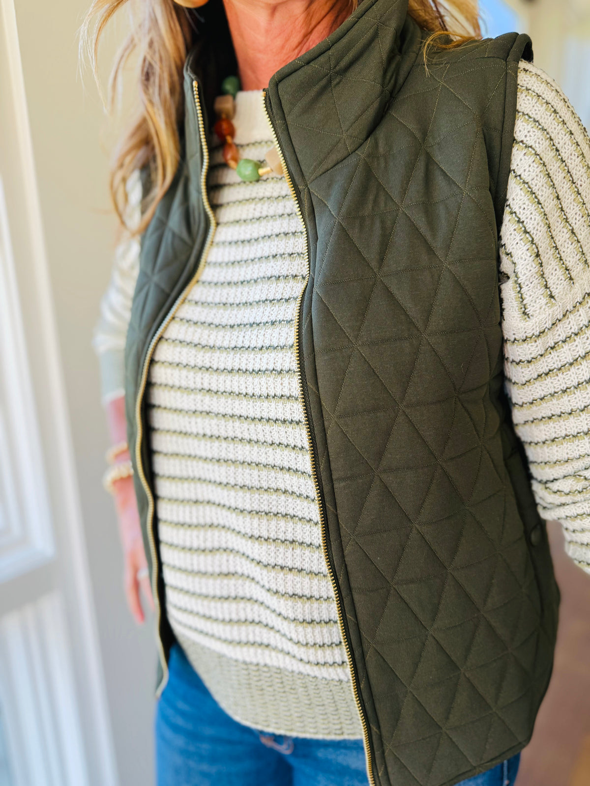 Close-up of the Rowan dark olive quilted vest showing its stand collar, geometric stitching and zip-front closure.