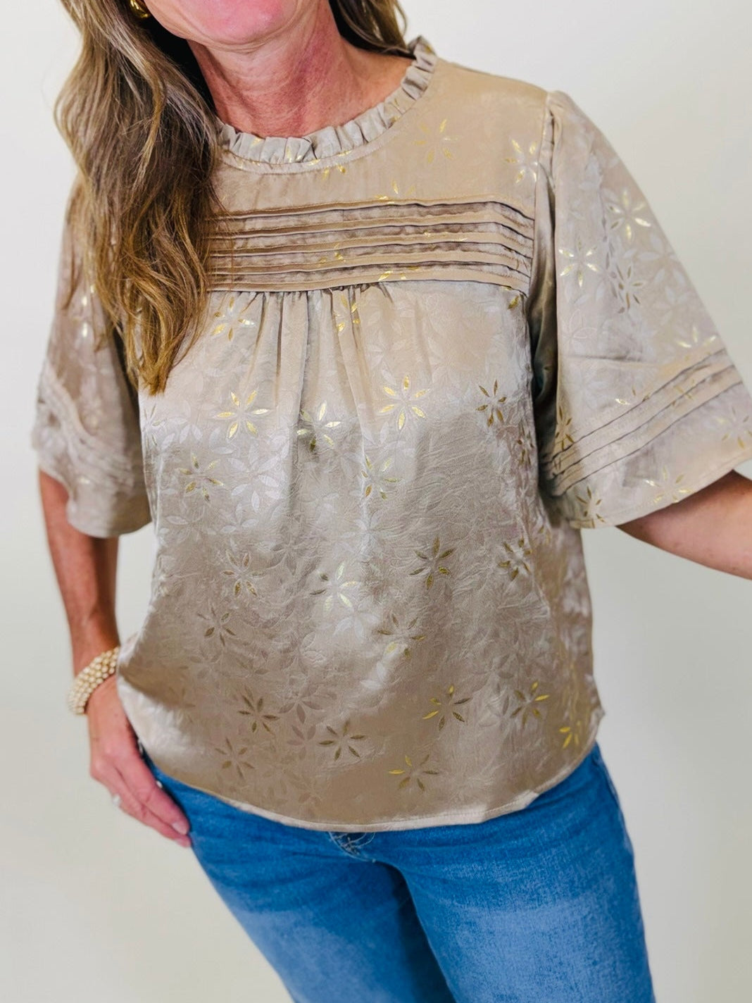 Close-up of the Serenity tan blouse showing its floral texture, pintuck detailing, ruffled neckline and wide sleeves.