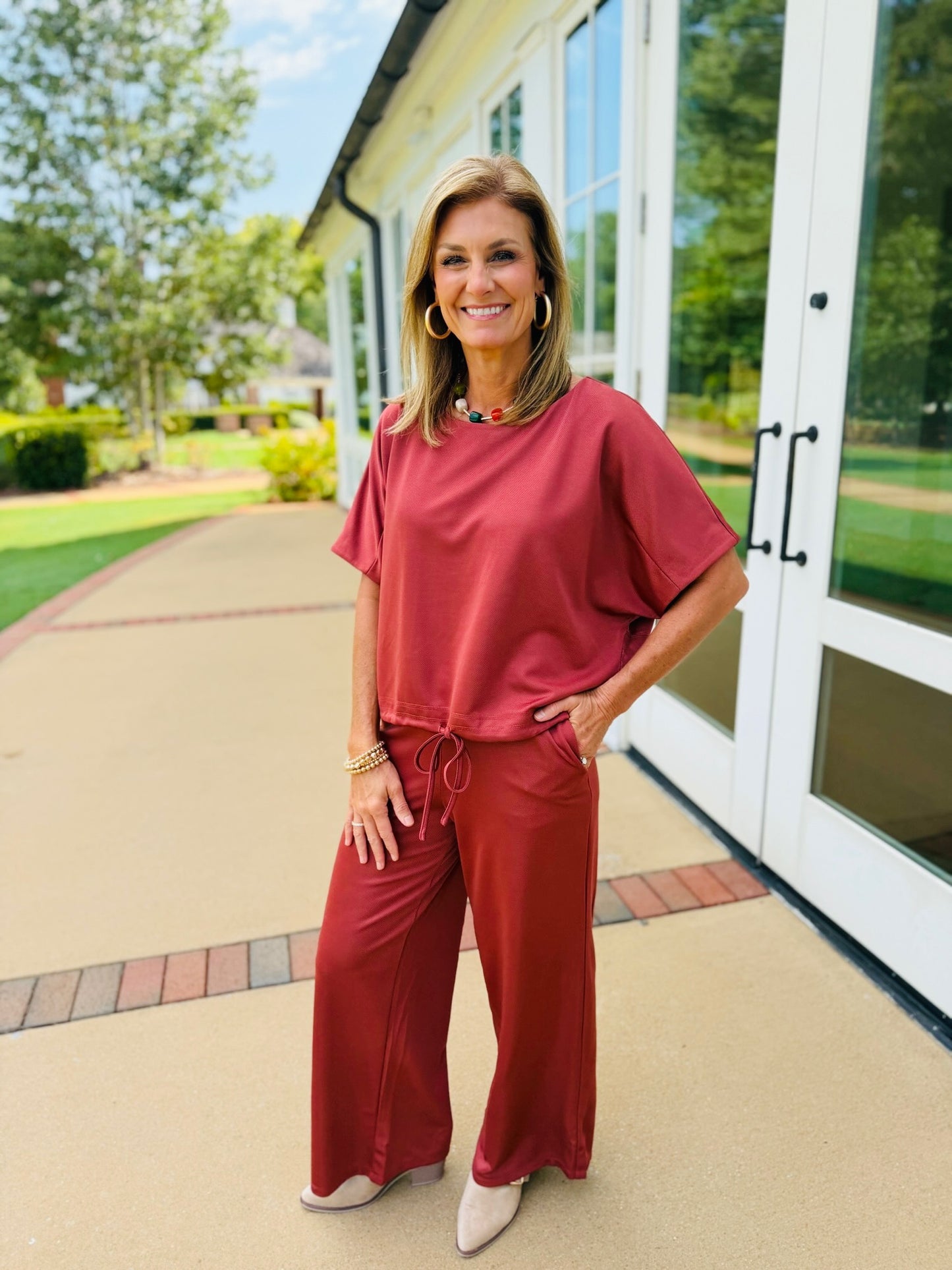 Ginny wearing the Sophia rust wide-leg pants with the matching short-sleeve drawstring-hem top and cream heels