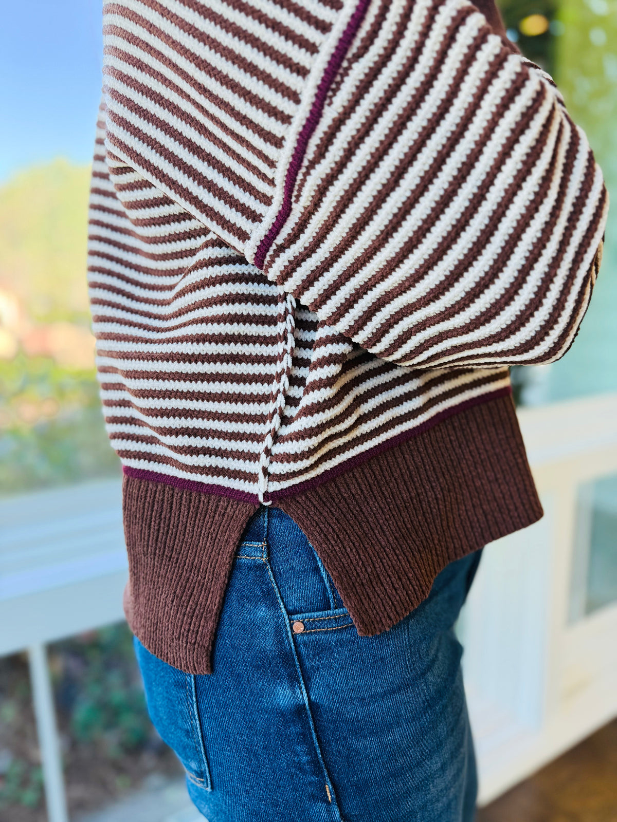 Side view of the Tess chocolate striped sweater showing its contrast seams, ribbed trim and split high-low hem.