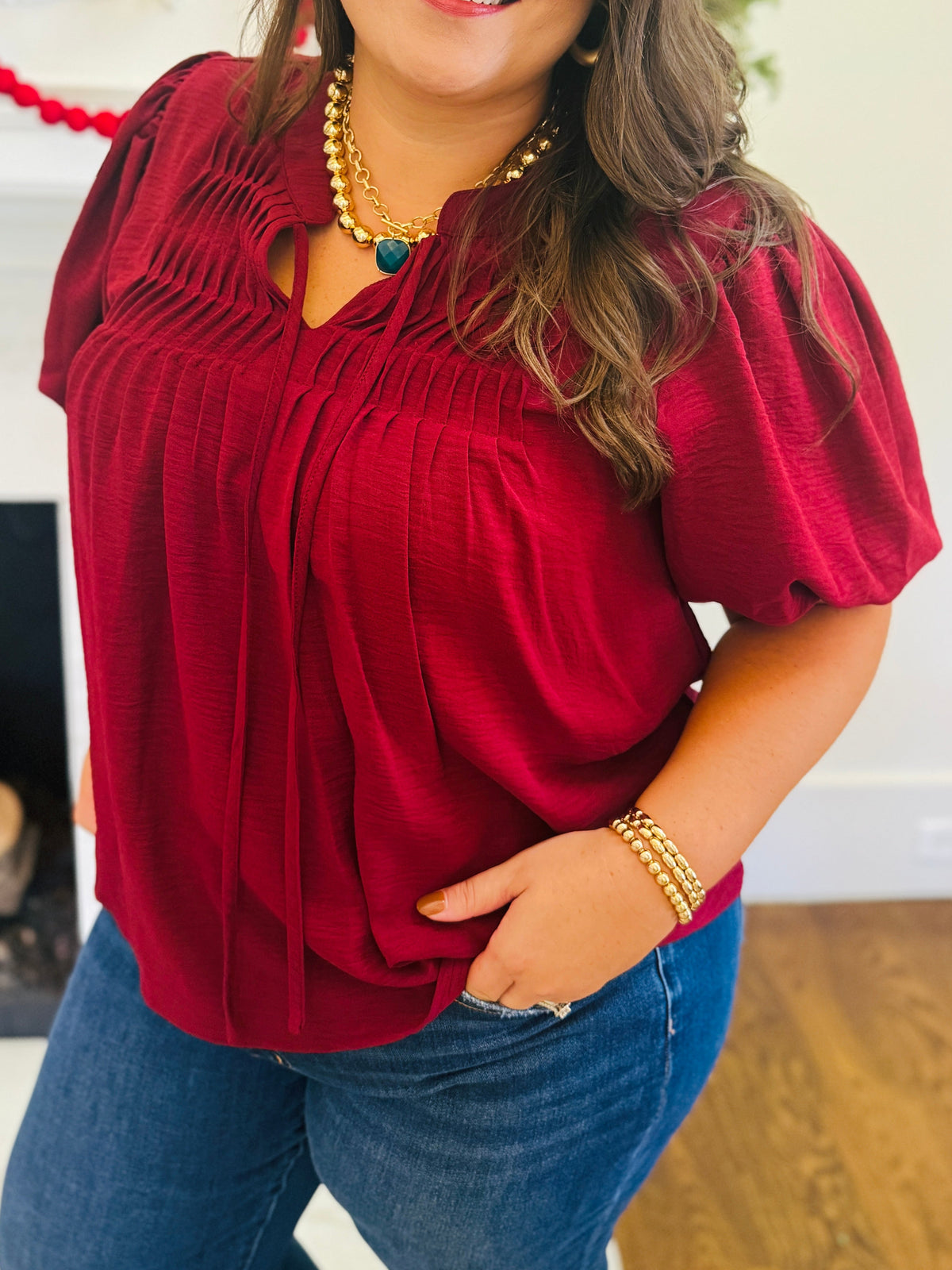 Close-up of the Vera burgundy blouse showing its pintuck front, split neckline, tie accents and puff sleeve.