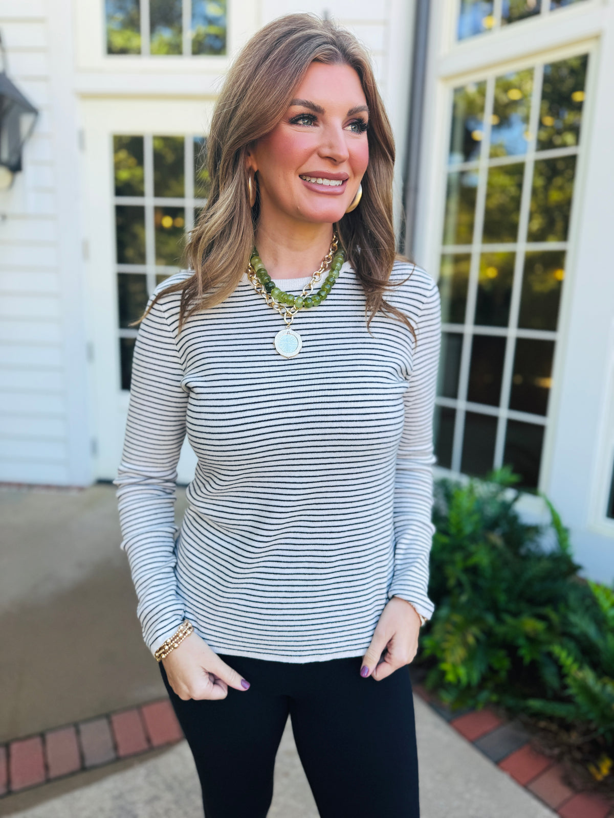 Morgan wearing the Veronica ivory and black striped ribbed top with black pants and layered necklaces.