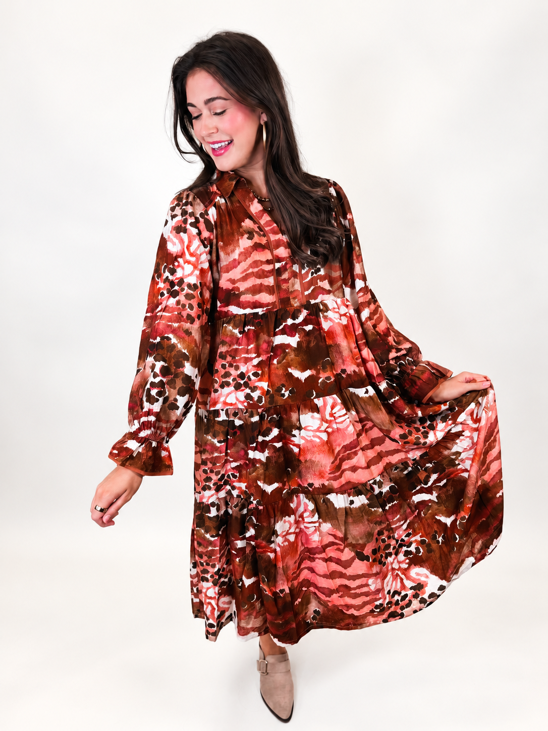 Lacey holding out the tiered skirt of the Victoria midi dress to show its rust multicolor abstract print and flowing silhouette.